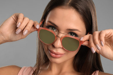 Beautiful young woman wearing sunglasses on grey background, closeup