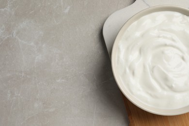 Photo of Bowl of fresh yogurt on grey table, top view. Space for text