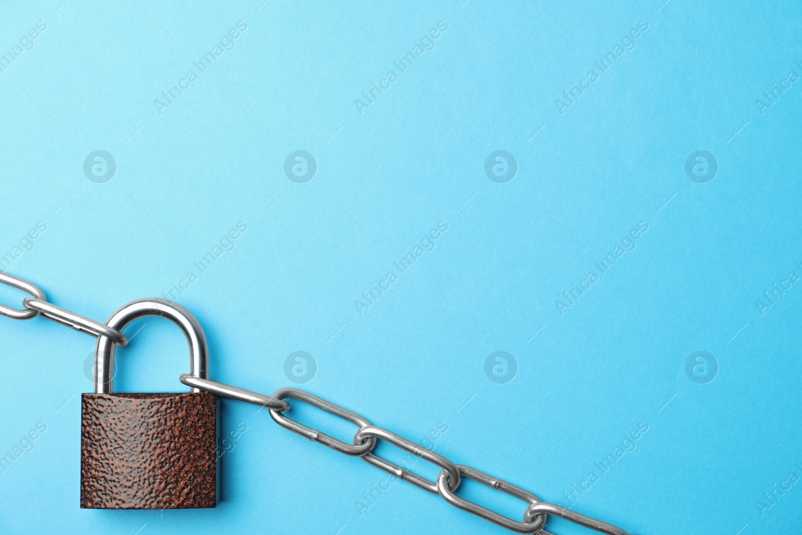 Photo of Steel padlock, chain and space for text on light blue background, top view. Safety concept