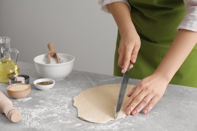 Photo of Woman cutting dough at light grey marble table, closeup. Cooking grissini
