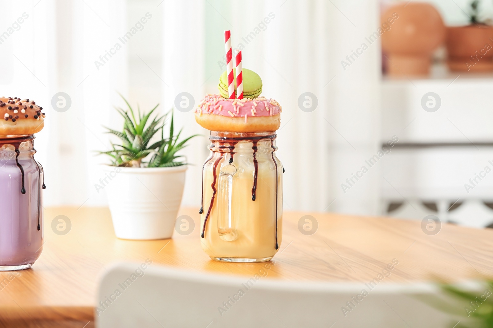 Photo of Mason jar with delicious milk shake on table against blurred background