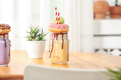 Mason jar with delicious milk shake on table against blurred background