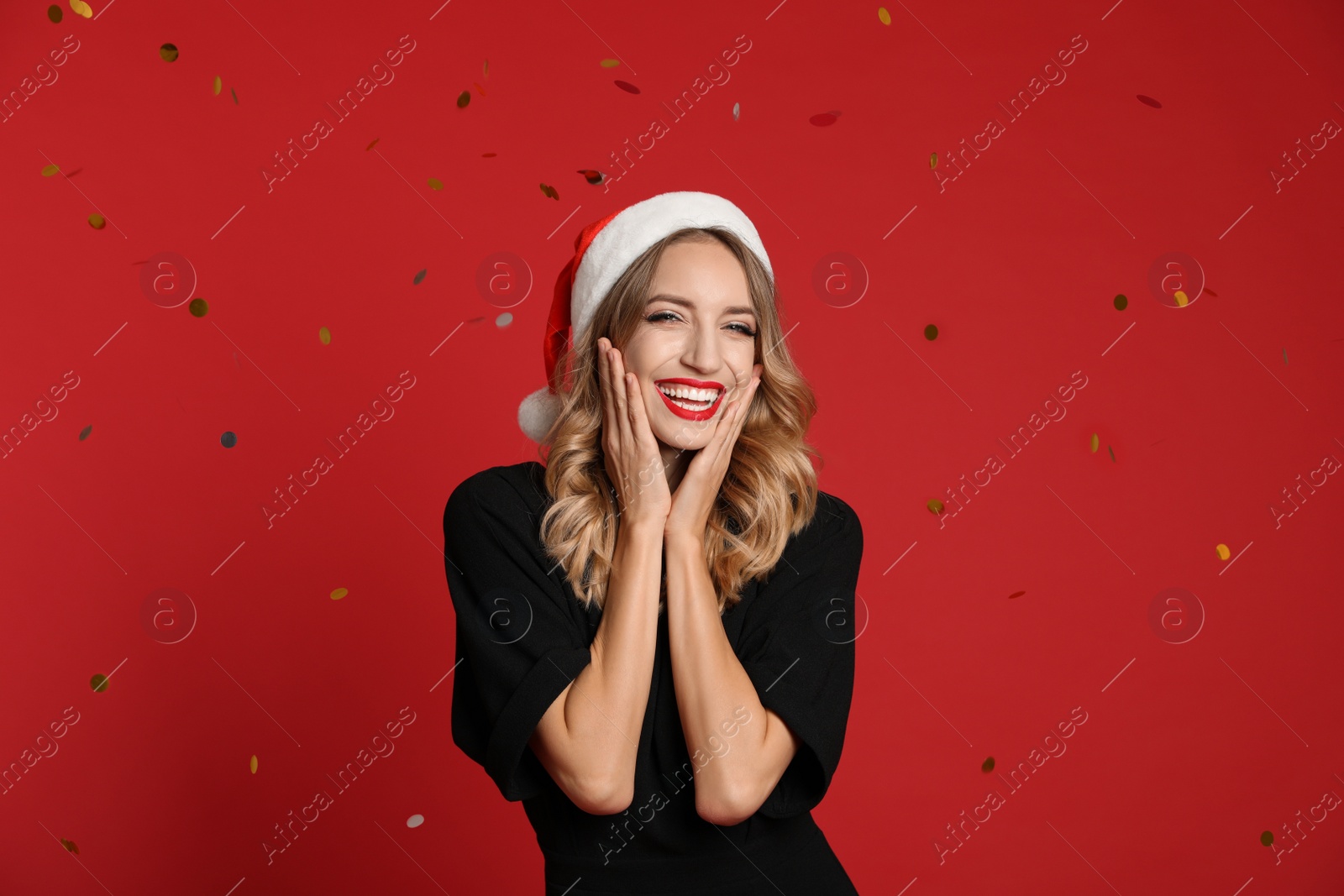 Photo of Happy young woman wearing Santa hat and confetti on red background. Christmas celebration