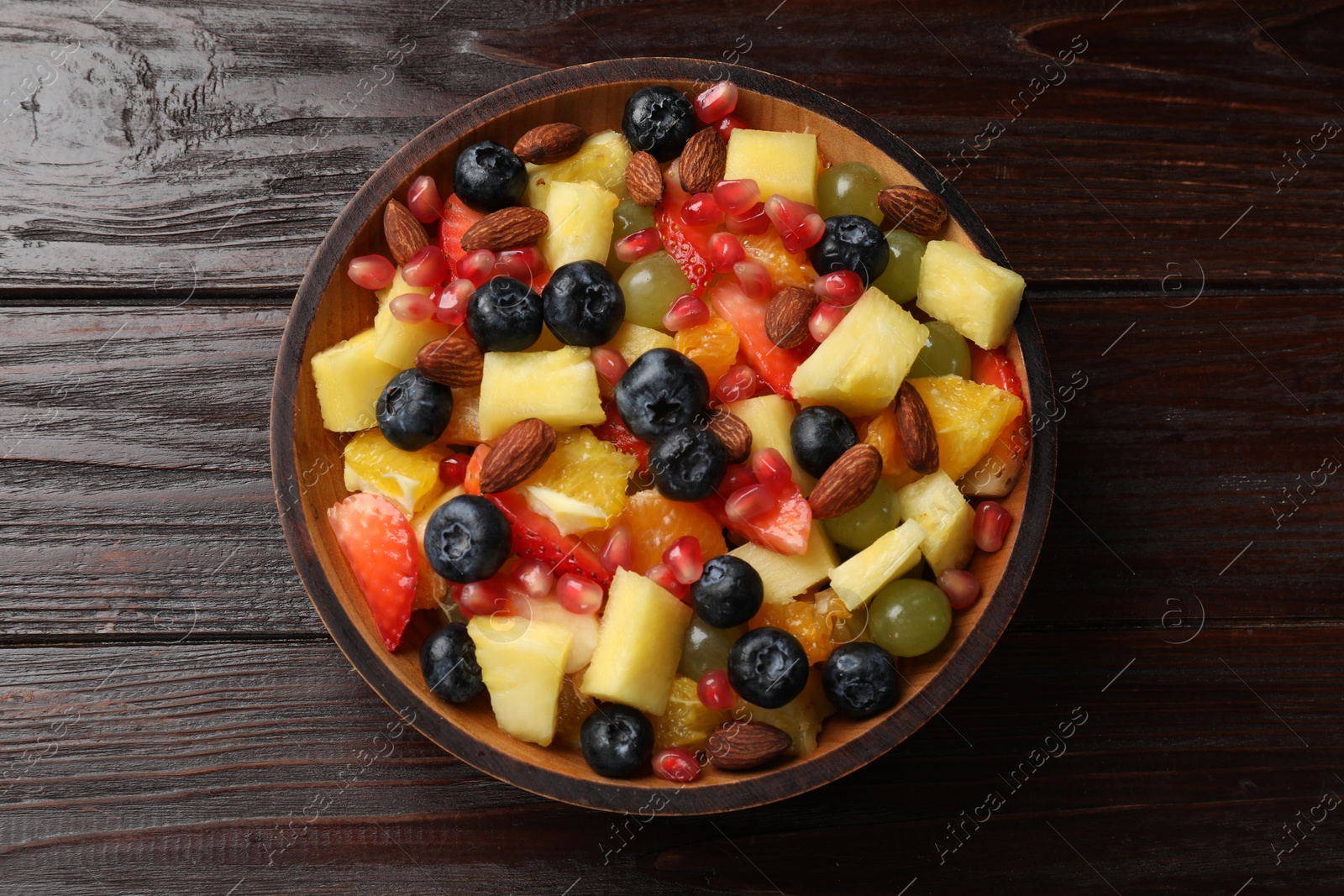 Photo of Delicious fruit salad in bowl on wooden table, top view