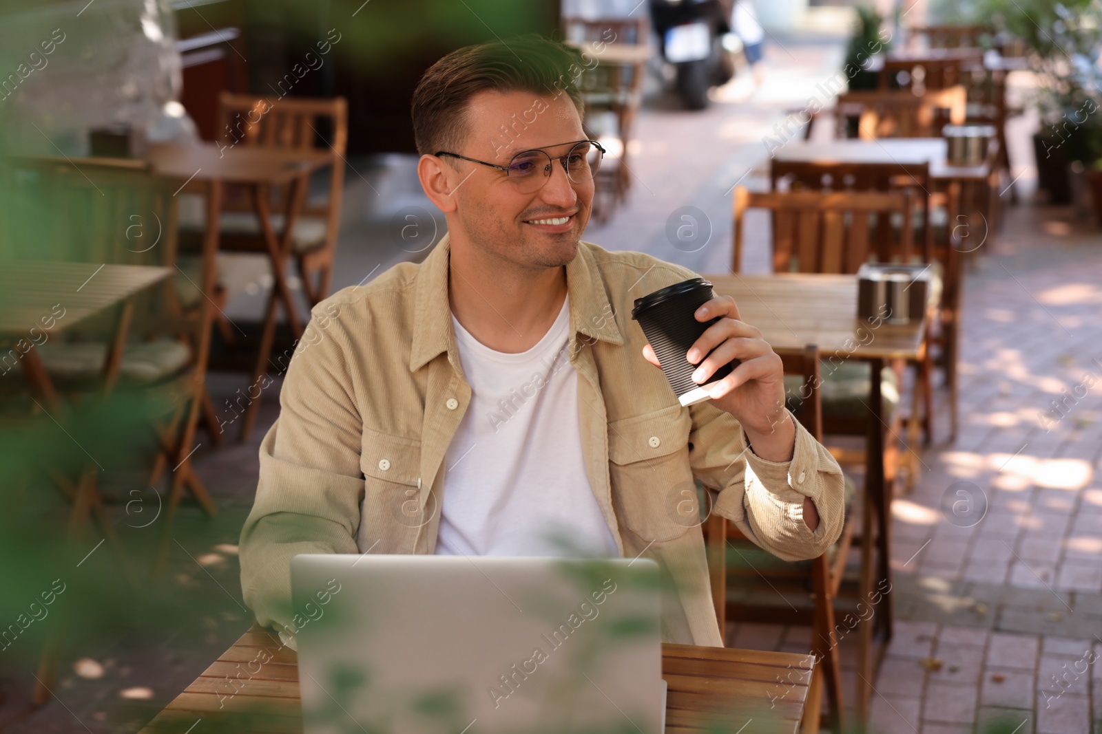 Photo of Handsome man with cup of coffee working on laptop at table in outdoor cafe