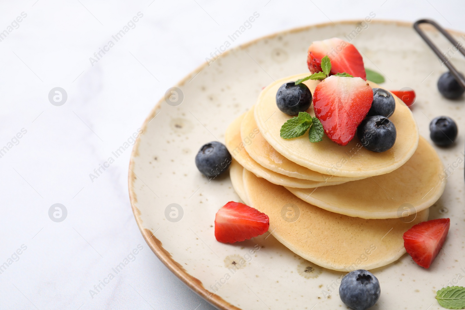 Photo of Delicious pancakes with berries and mint on white marble table, closeup. Space for text