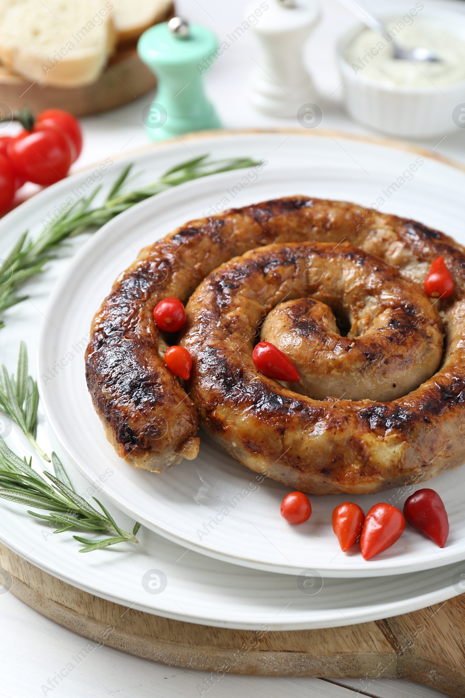Photo of Tasty homemade sausages with peppers and rosemary on white table, closeup