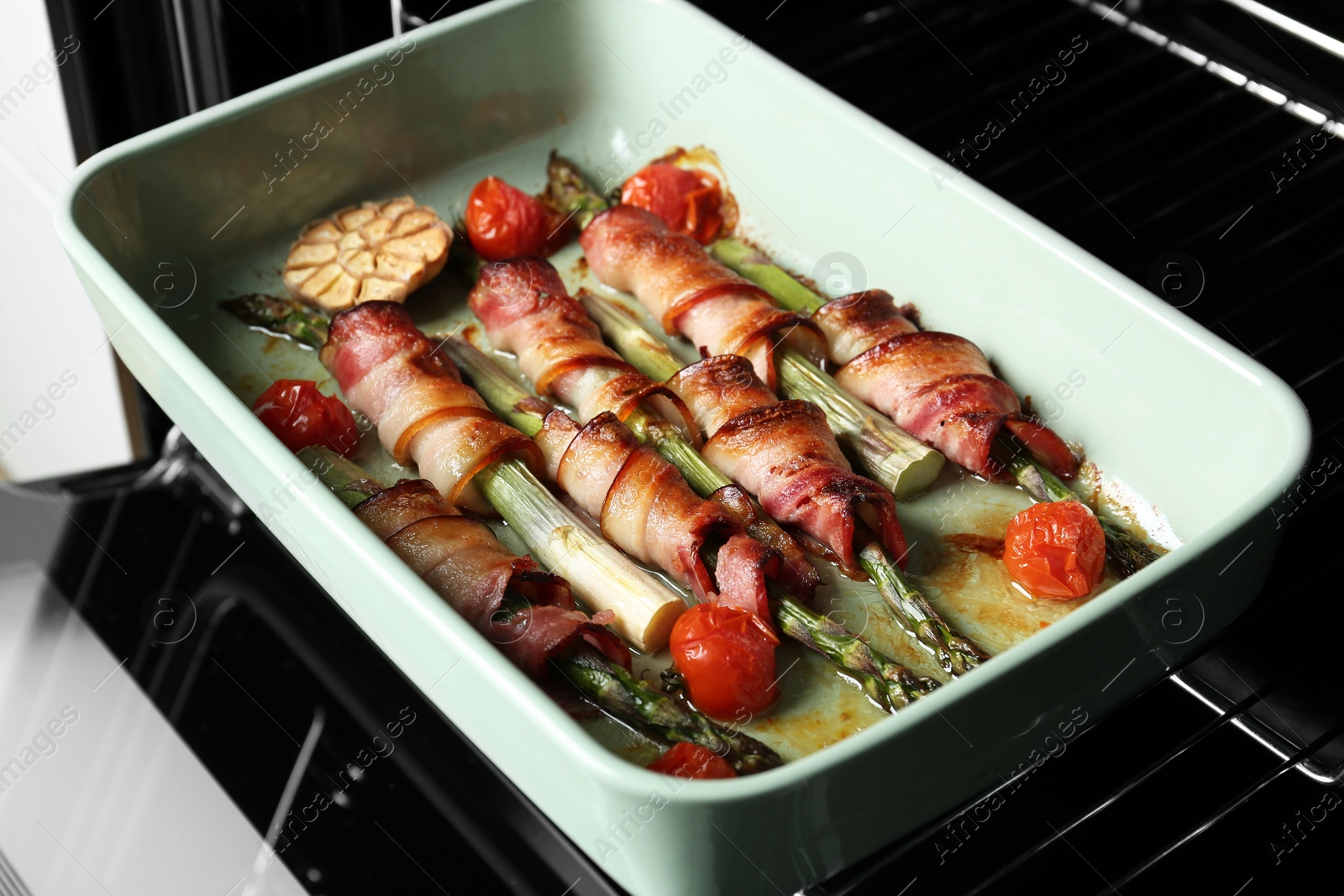 Photo of Bacon wrapped asparagus in baking dish on oven rack, closeup