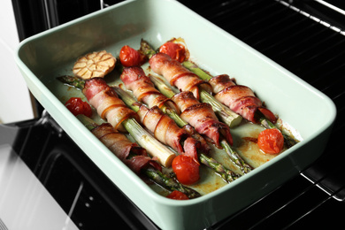 Bacon wrapped asparagus in baking dish on oven rack, closeup