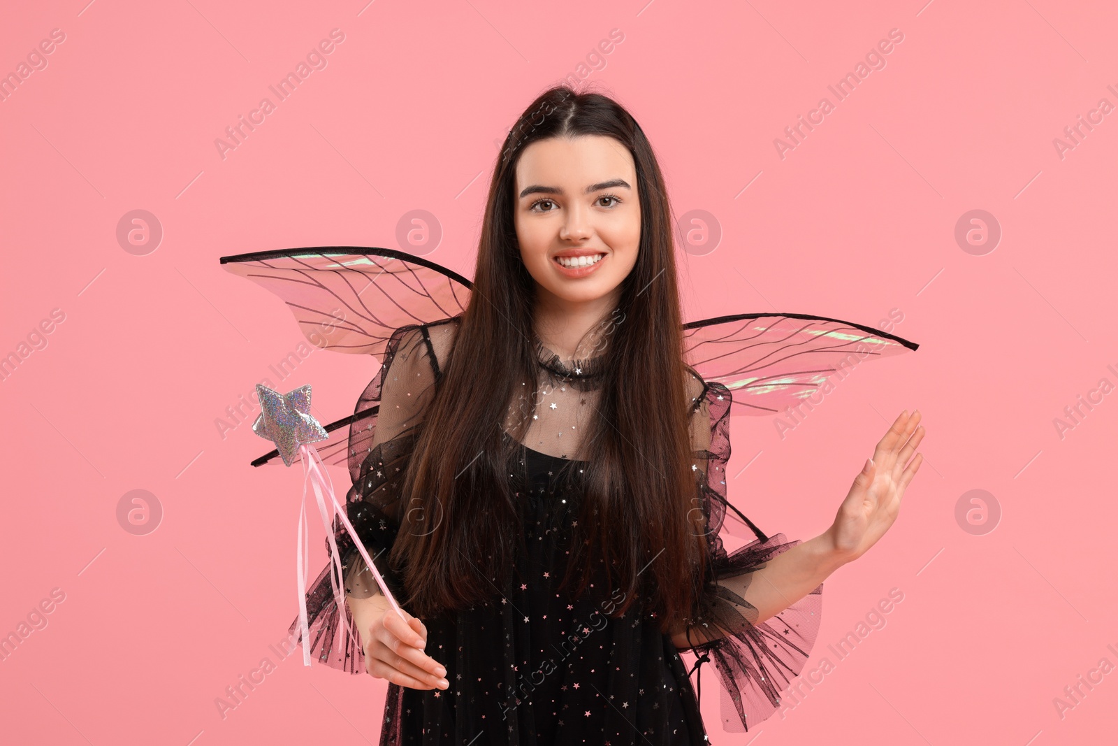 Photo of Beautiful girl in fairy costume with wings and magic wand on pink background