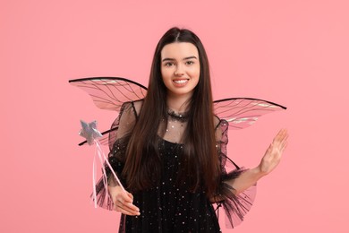 Beautiful girl in fairy costume with wings and magic wand on pink background