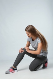 Full length portrait of sportswoman having knee problems on grey background