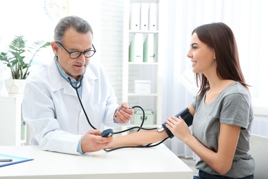 Young woman visiting doctor in hospital. Measuring blood pressure and checking pulse