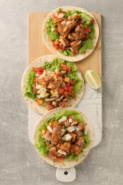Photo of Delicious tacos with vegetables, meat and lime on grey textured table, top view