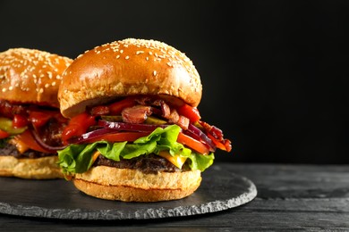 Photo of Tasty burgers on black wooden table, closeup with space for text. Fast food