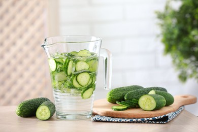 Refreshing cucumber water in jug and vegetables on light wooden table