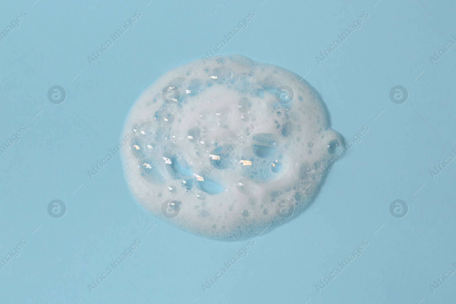 Photo of Foam on light blue background, top view. Face cleanser, skin care cosmetic
