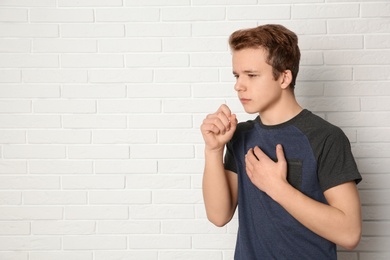 Photo of Teenage boy suffering from cough near brick wall. Space for text
