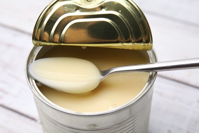 Photo of Tasty condensed milk and spoon in tin can at white table, closeup