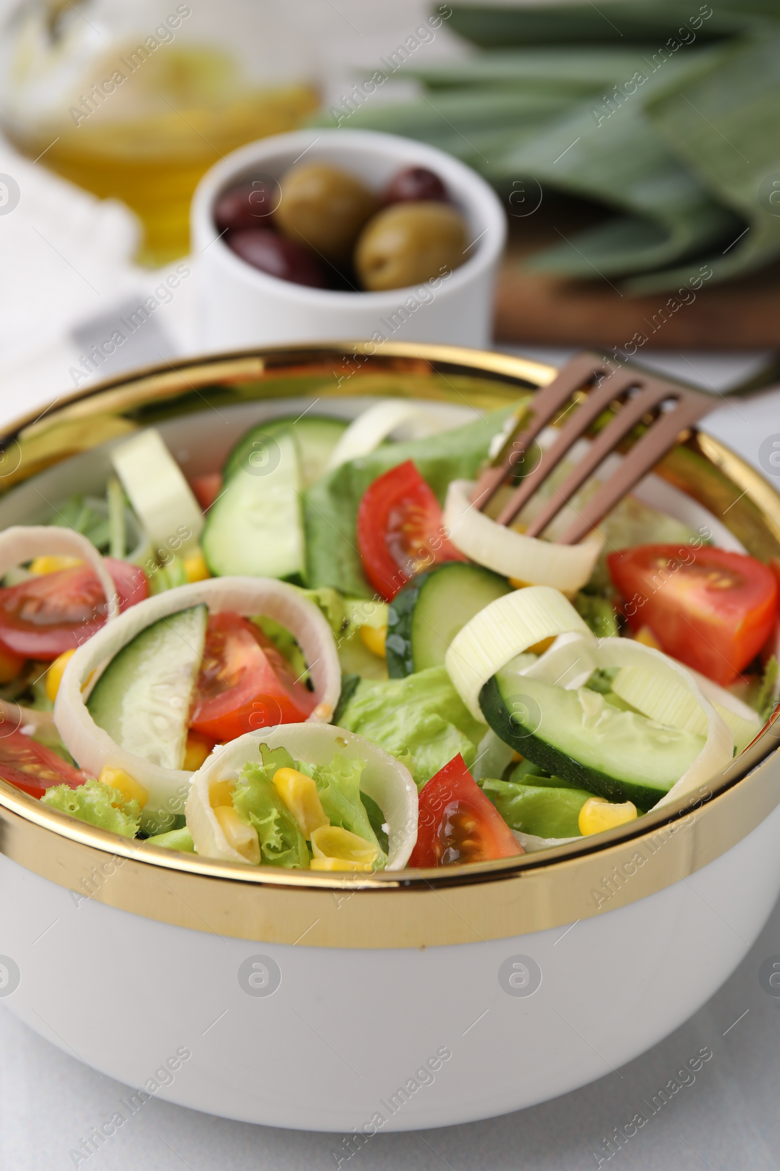 Photo of Bowl of tasty salad with leek, tomatoes and cucumbers on white table, closeup