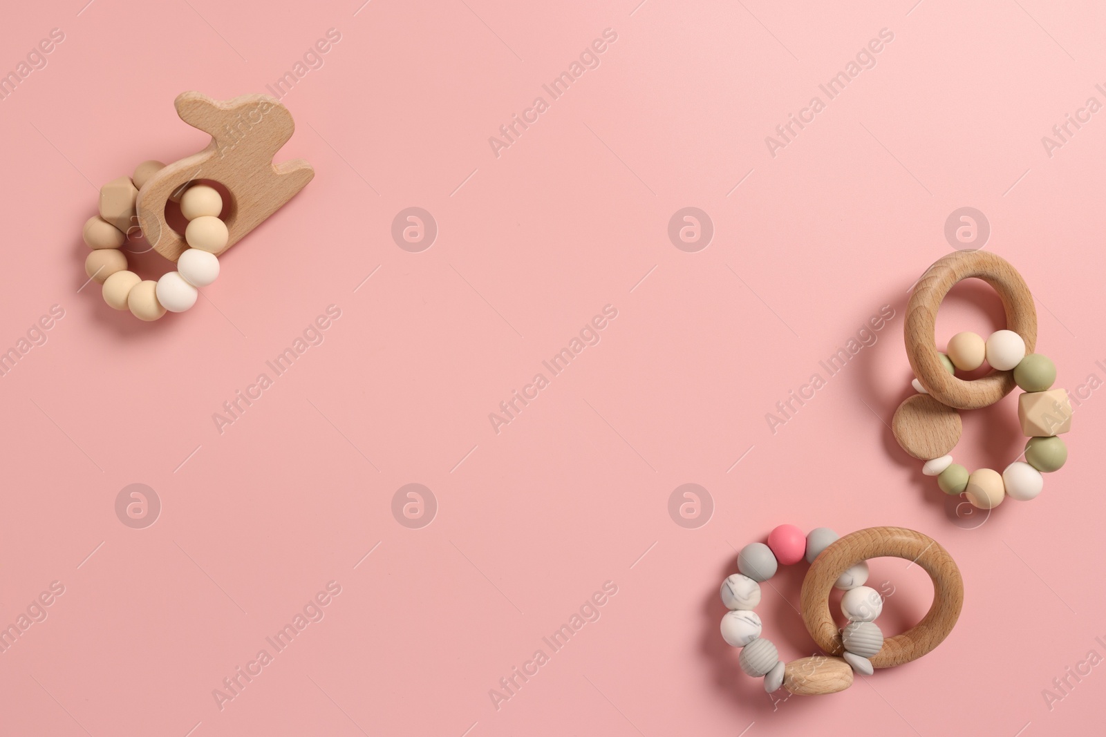 Photo of Baby accessories. Wooden rattles on pink background, flat lay. Space for text