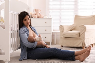 Photo of Tired young mother sleeping while breastfeeding her baby in children's room