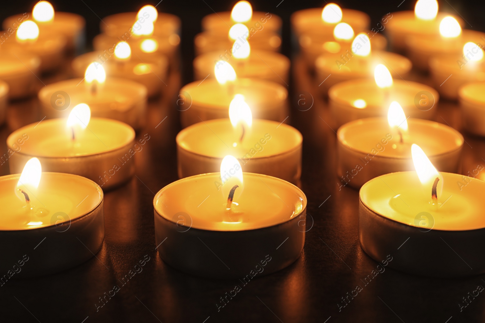 Photo of Wax candles burning on table in darkness, closeup