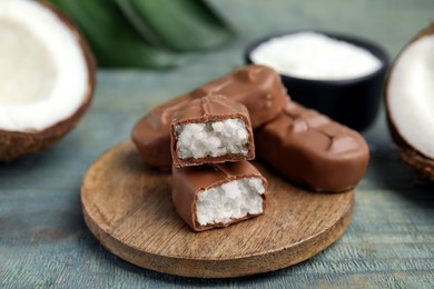 Photo of Delicious milk chocolate candy bars with coconut filling on blue wooden table, closeup