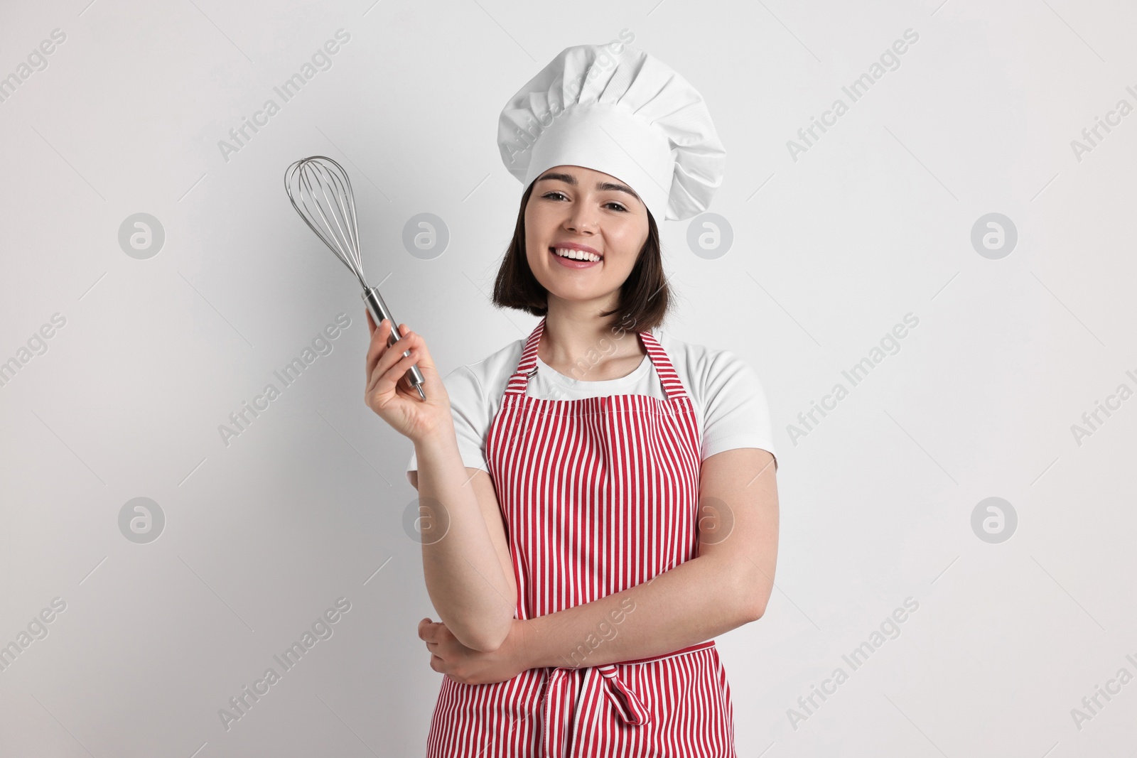 Photo of Happy confectioner holding whisk on light grey background