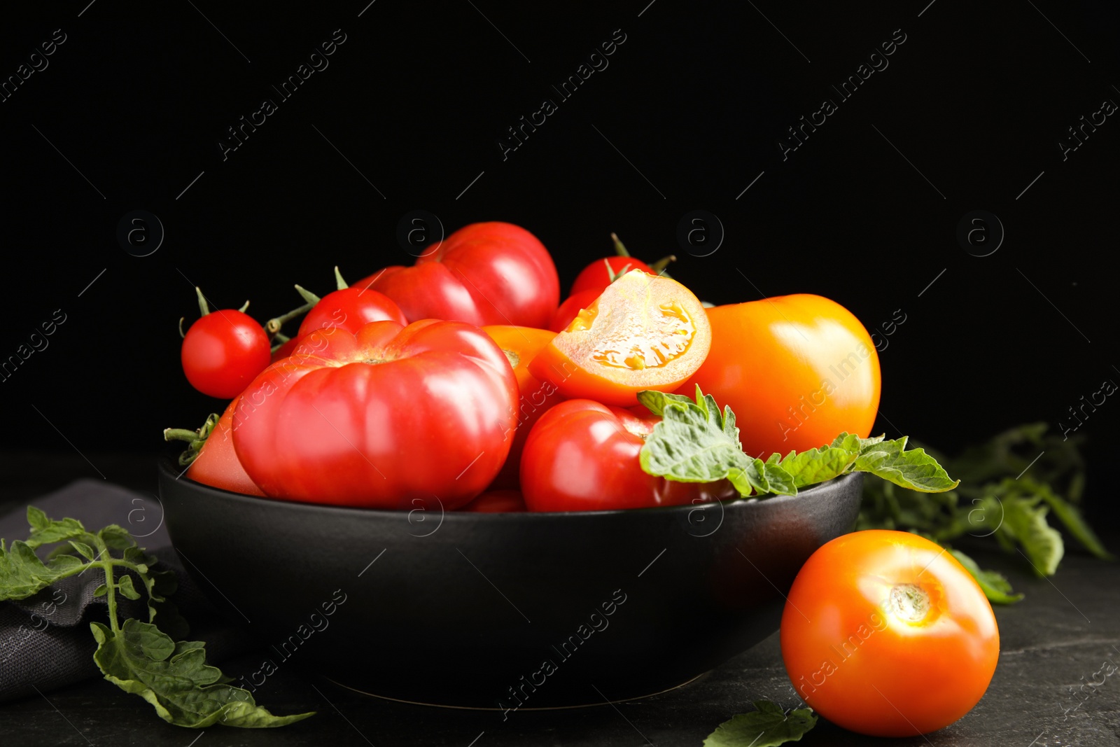 Photo of Many different ripe tomatoes with leaves on black table