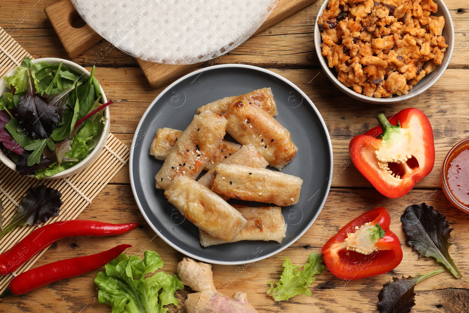 Photo of Tasty fried spring rolls and ingredients on wooden table, flat lay