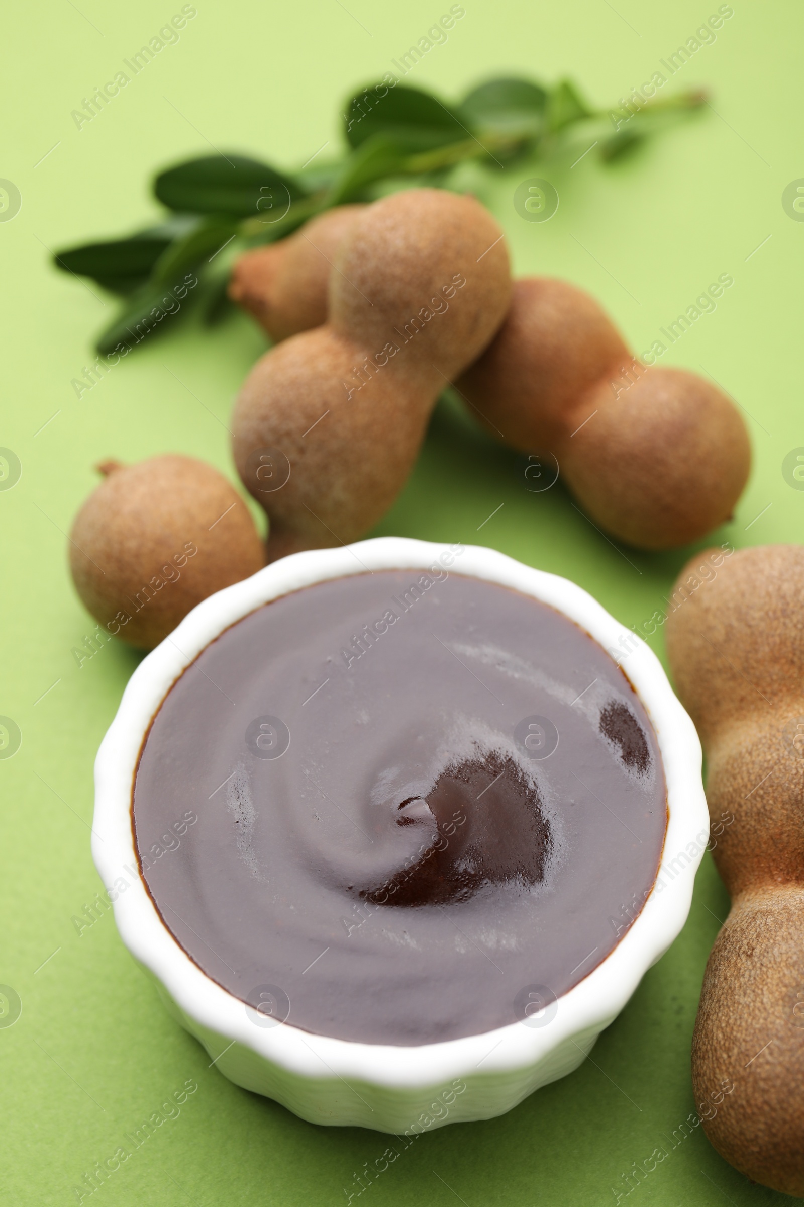 Bowl of tasty tamarind sauce and fresh pods on light green table Photo of Bowl of tasty tamarind sauce and fresh pods on light green table