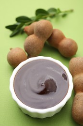 Photo of Bowl of tasty tamarind sauce and fresh pods on light green table