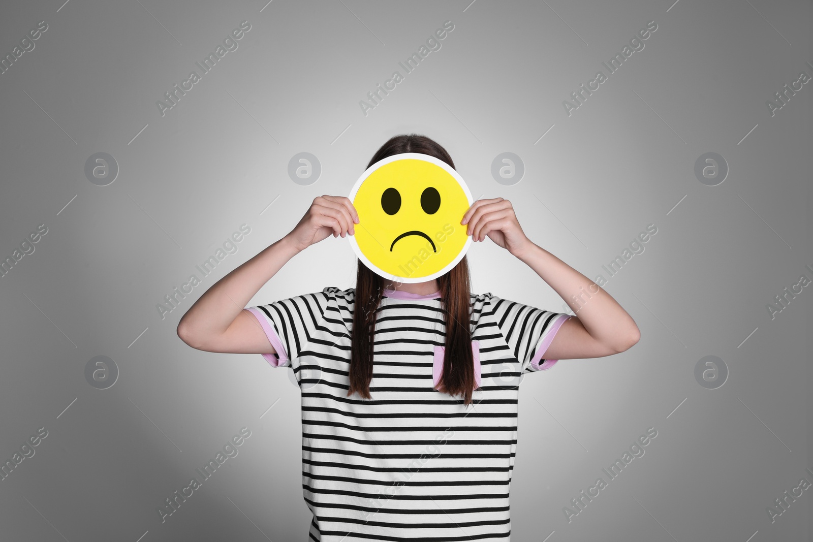 Image of Woman hiding behind card with sad face on grey background