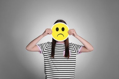 Woman hiding behind card with sad face on grey background