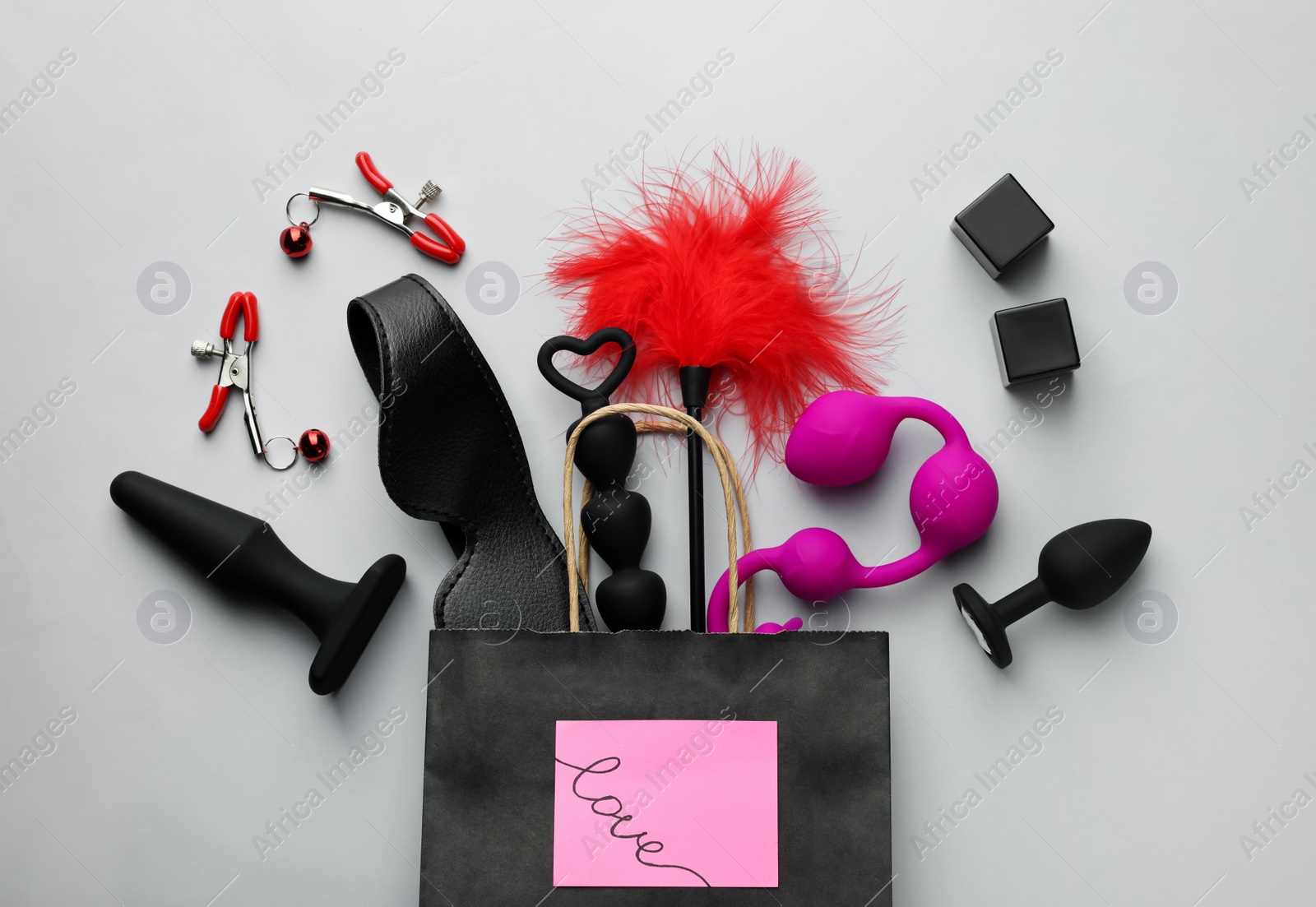 Photo of Paper shopping bag with different sex toys on white background, flat lay