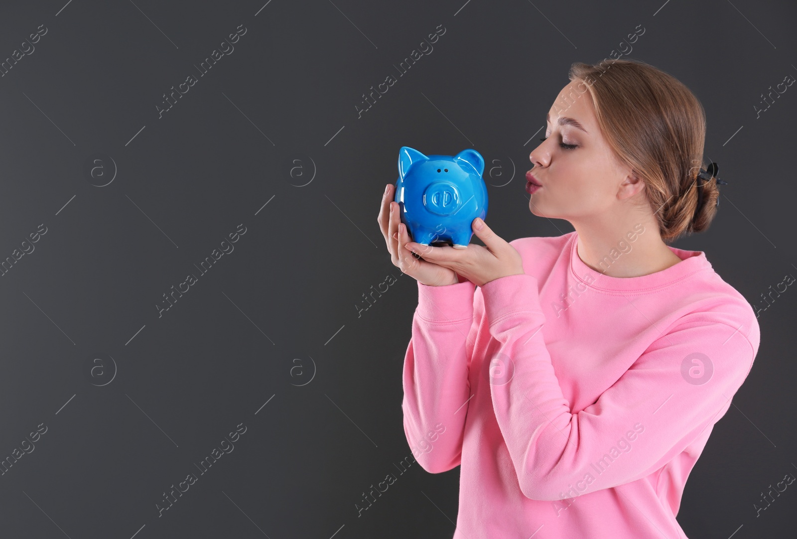 Photo of Happy young woman with piggy bank and space for text on grey background. Money saving