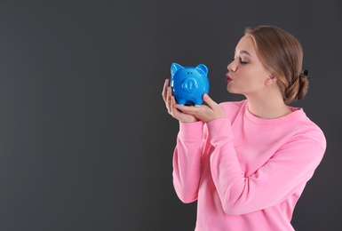 Happy young woman with piggy bank and space for text on grey background. Money saving