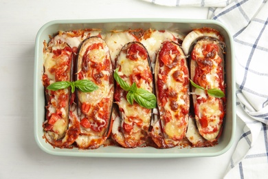 Photo of Baked eggplant with tomatoes, cheese and basil in dishware on white wooden table, flat lay