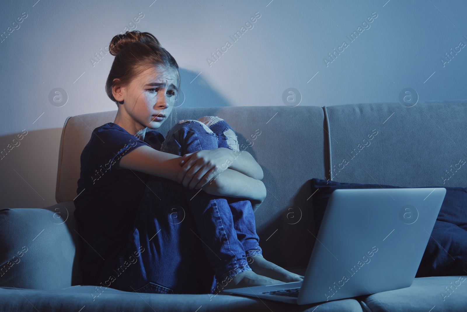 Photo of Frightened teenage girl with laptop on sofa in dark room. Danger of internet