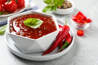 Photo of Spicy chili sauce with basil on light grey table