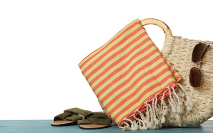 Photo of Beach bag with towel, slippers and sunglasses on light blue wooden surface against white background