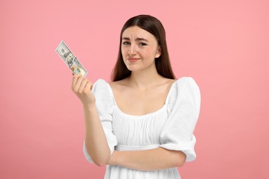 Sad woman with dollar banknote on pink background