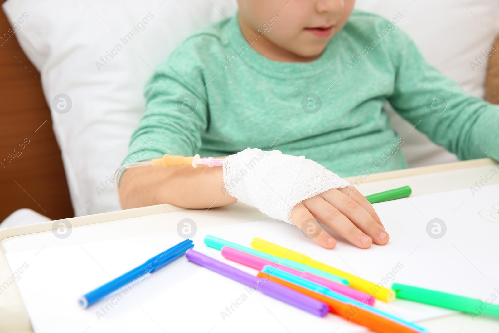 Photo of Little child with infusion drip drawing in hospital bed, closeup