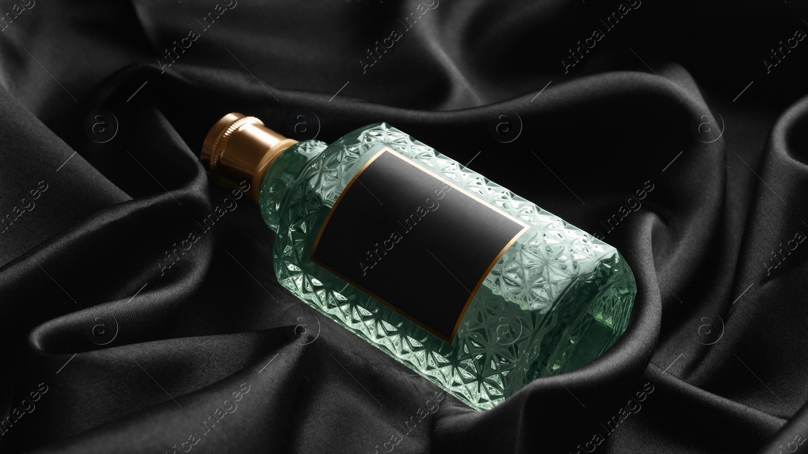 Photo of Luxury bottle of perfume on black silk, closeup