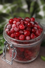 Photo of Frozen red cranberries in glass jar on brown table, closeup