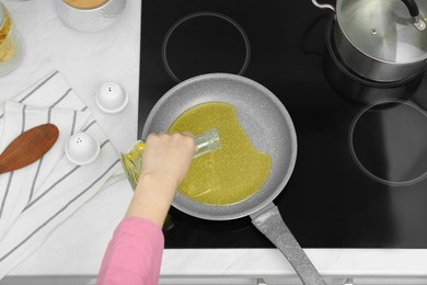 Photo of Woman pouring oil from jug into frying pan in kitchen, top view