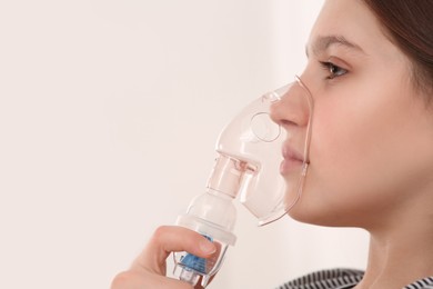 Photo of Cute girl using nebulizer for inhalation on white background, closeup. Space for text