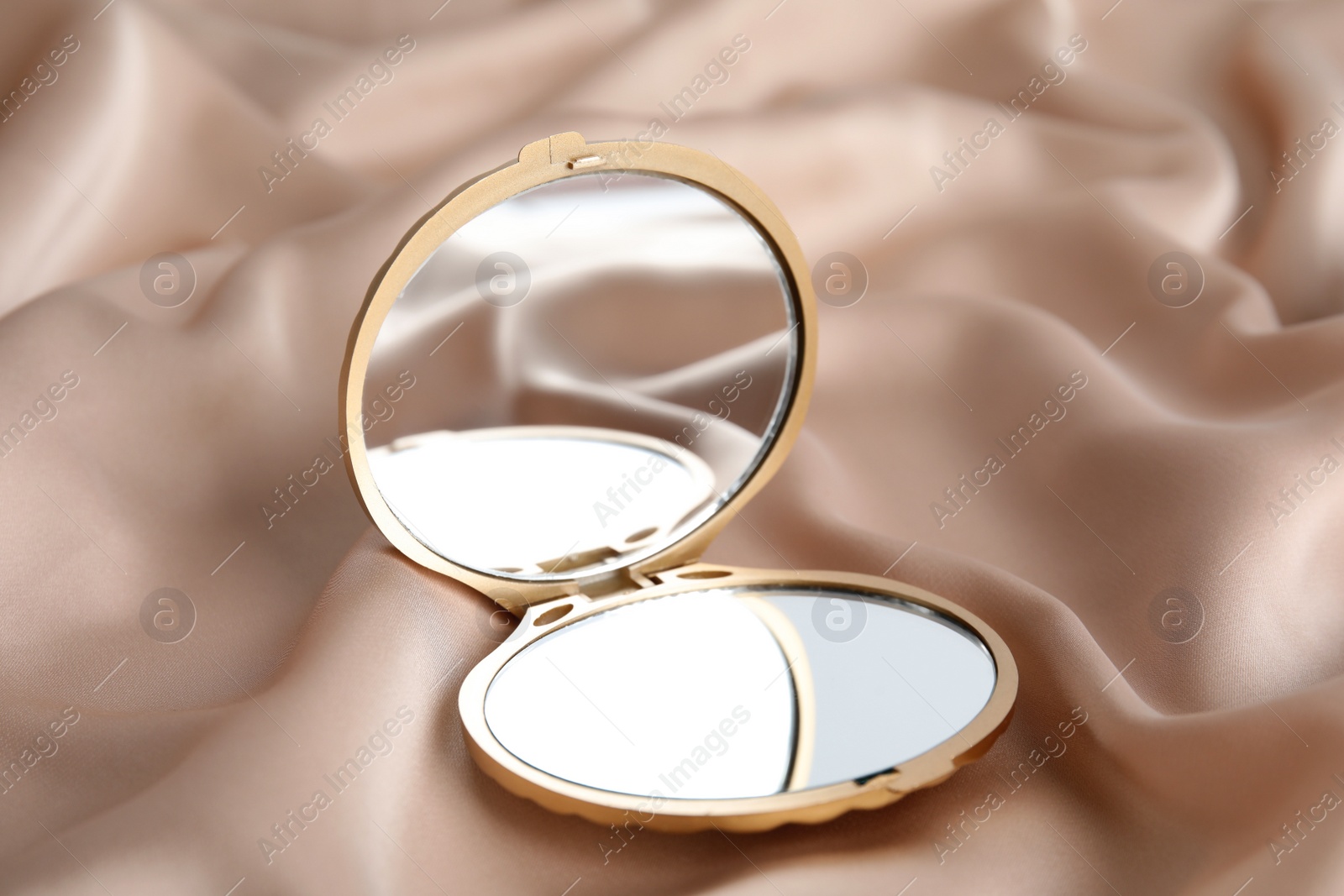 Photo of Bright cosmetic pocket mirror on rose gold fabric