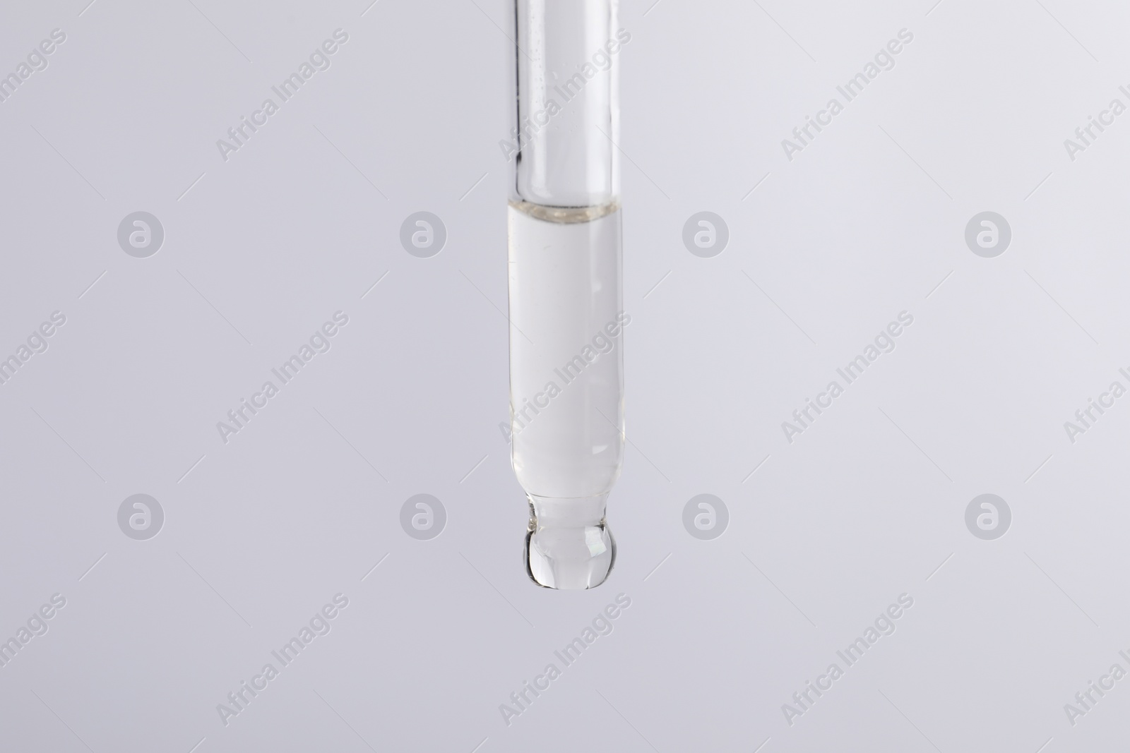 Photo of Dripping cosmetic serum from pipette on light grey background